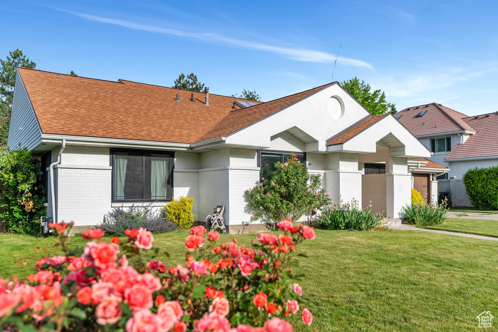 View of front of home with brick siding, a front yard, and a shingled roof