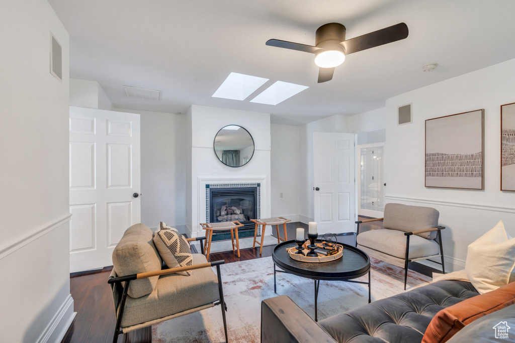 Living area featuring a skylight, wood finished floors, a ceiling fan, and baseboards