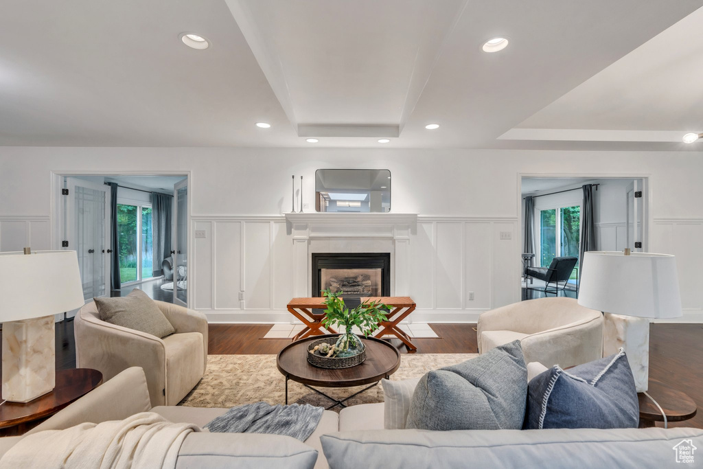 Living area featuring a decorative wall, a tray ceiling, wood finished floors, a fireplace, and a wainscoted wall