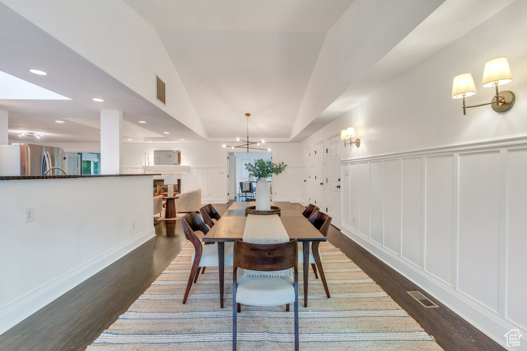 Dining area with dark wood-style flooring, a decorative wall, a chandelier, recessed lighting, and a wainscoted wall