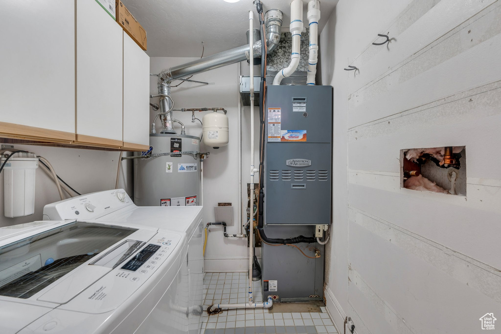 Laundry room featuring cabinet space, washing machine and dryer, water heater, tile patterned floors, and baseboards