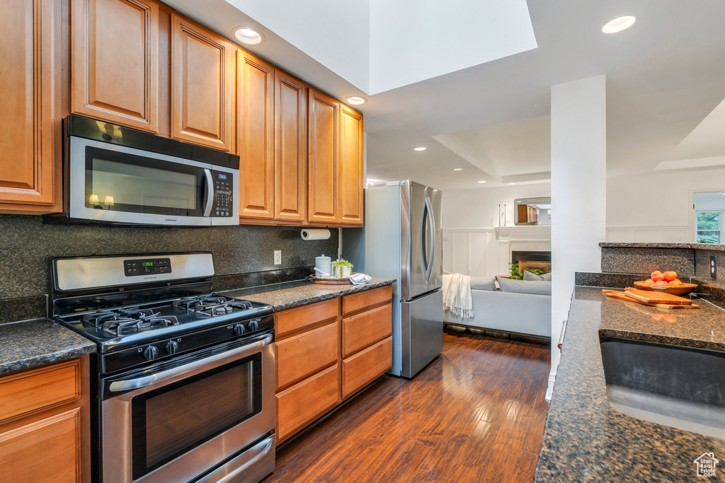 Kitchen with appliances with stainless steel finishes, dark wood-style floors, tasteful backsplash, recessed lighting, and dark stone counters