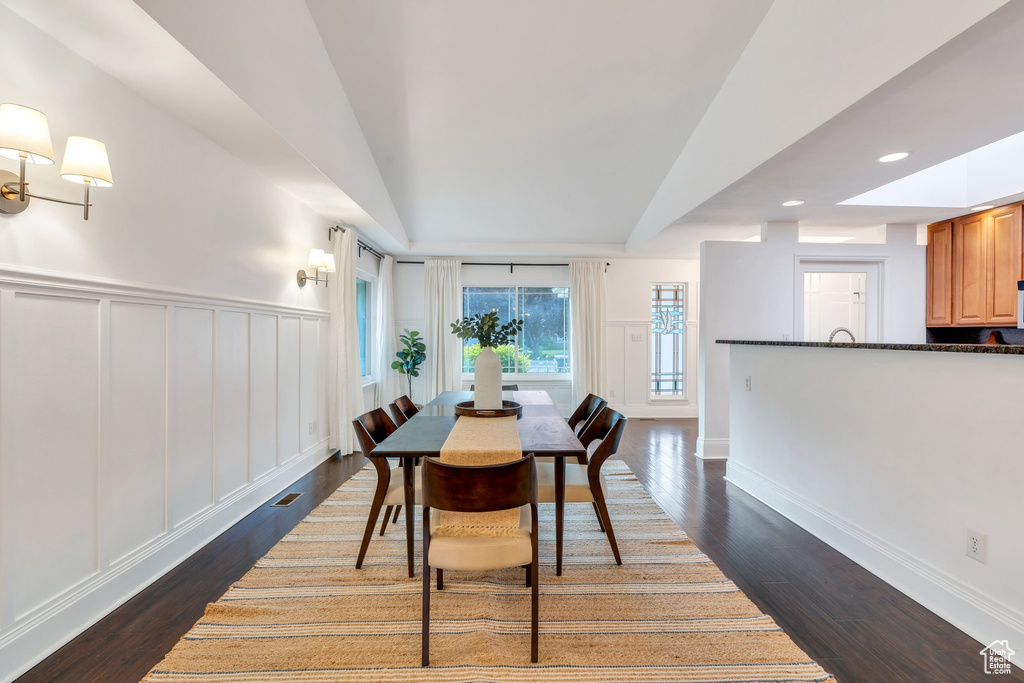 Dining area with a decorative wall, dark wood-type flooring, wainscoting, and recessed lighting