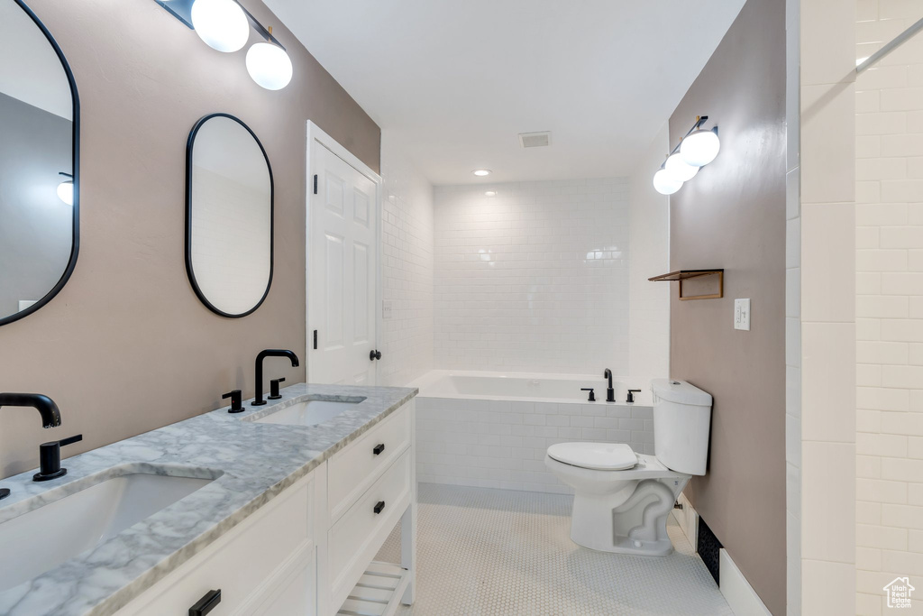 Full bathroom featuring toilet, tiled tub, double vanity, and tile patterned flooring