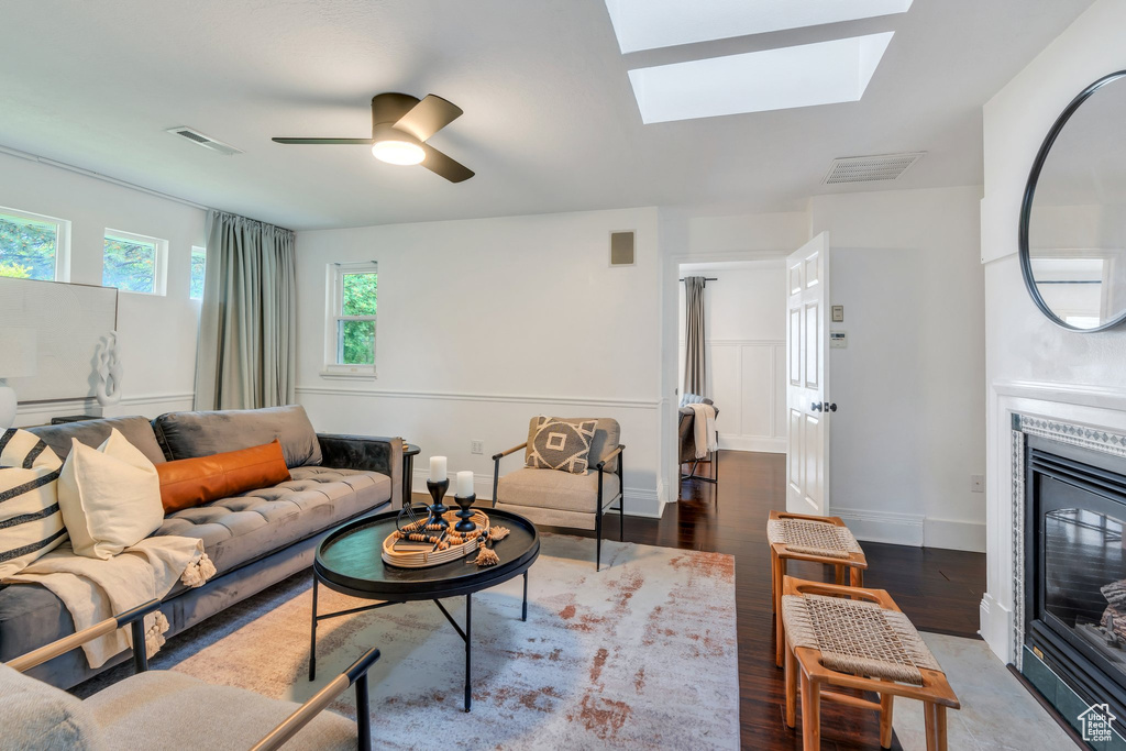 Living room with a glass covered fireplace, wood finished floors, ceiling fan, a skylight, and baseboards