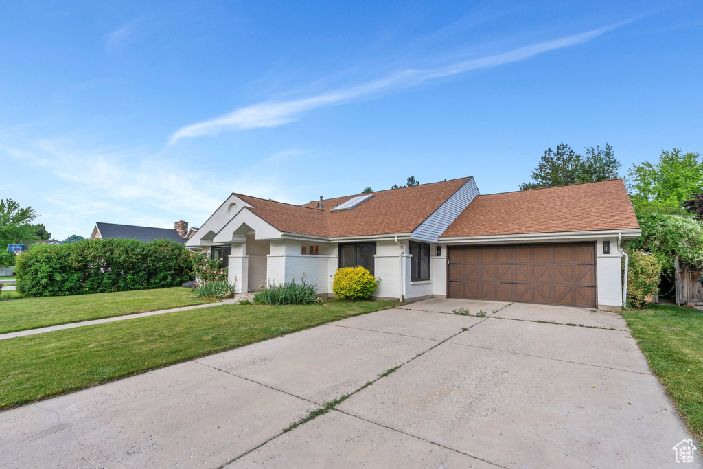 Ranch-style home featuring a garage, a front lawn, driveway, and stucco siding