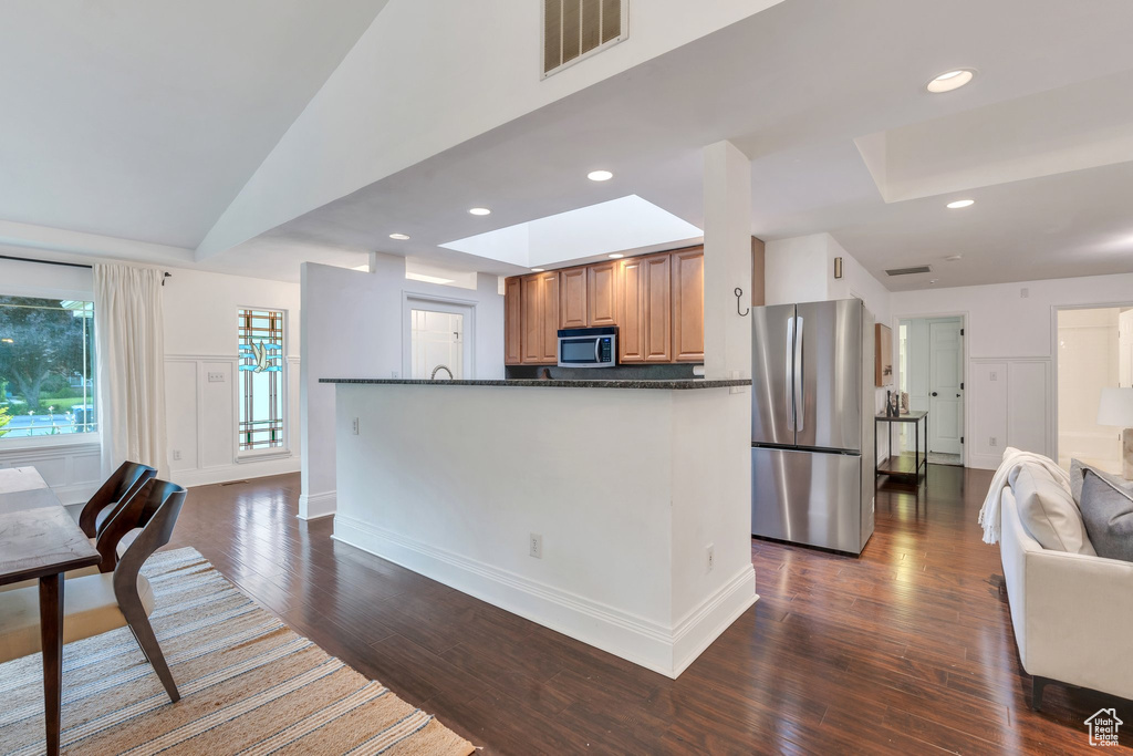 Kitchen with stainless steel appliances, dark wood-style flooring, a skylight, open floor plan, and brown cabinets