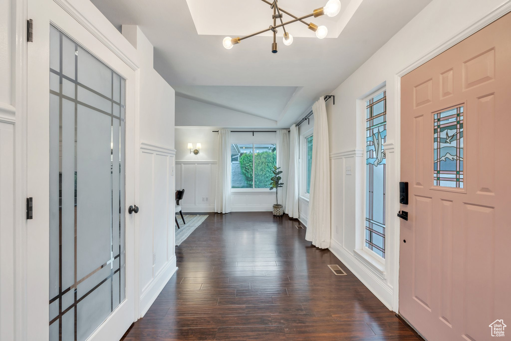 Entryway with a decorative wall, a chandelier, vaulted ceiling, dark wood-style floors, and wainscoting