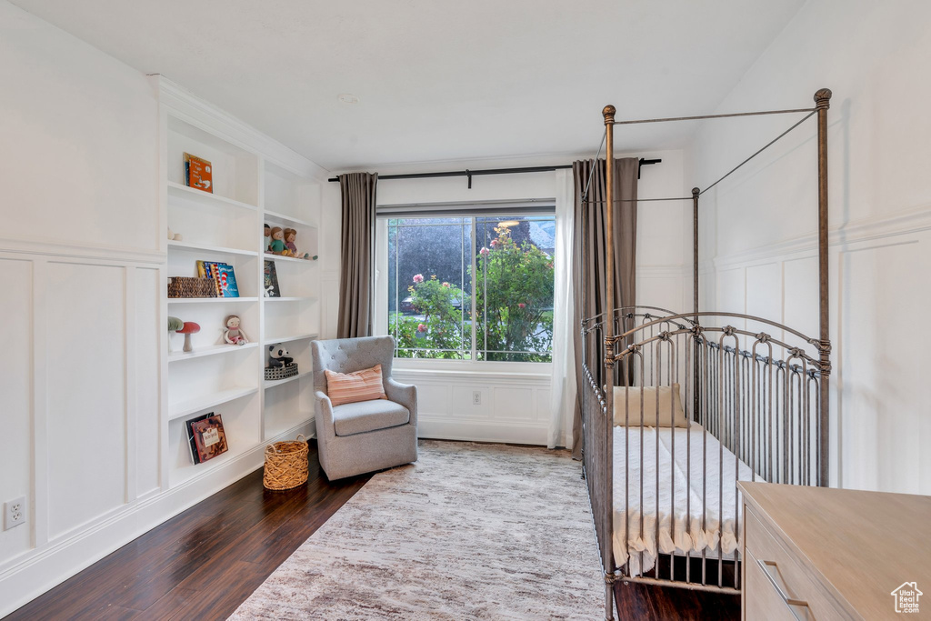 Bedroom featuring a decorative wall, dark wood-style flooring, and a wainscoted wall