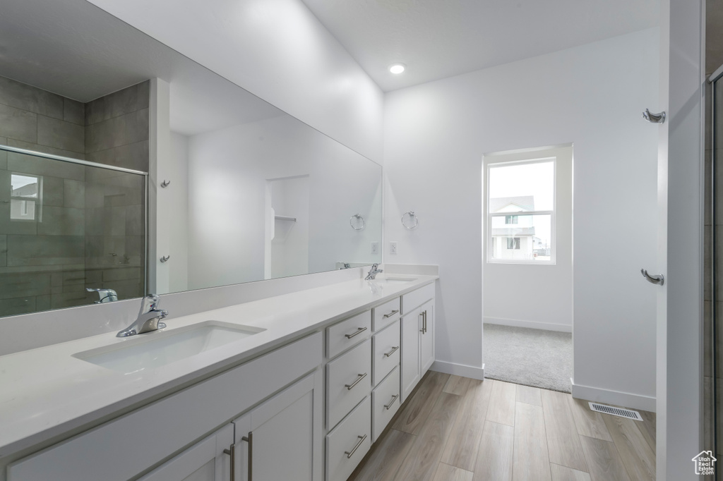 Full bathroom with double vanity, a shower stall, wood finished floors, recessed lighting, and baseboards