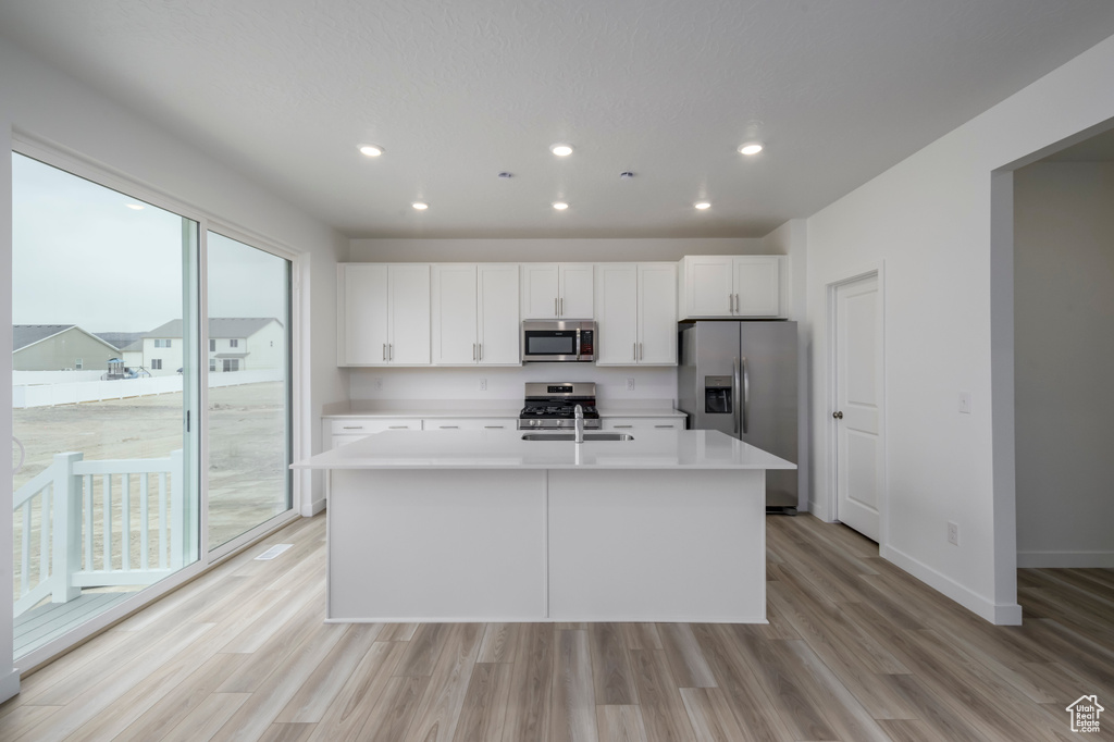 Kitchen with stainless steel appliances, a sink, recessed lighting, a center island with sink, and light countertops