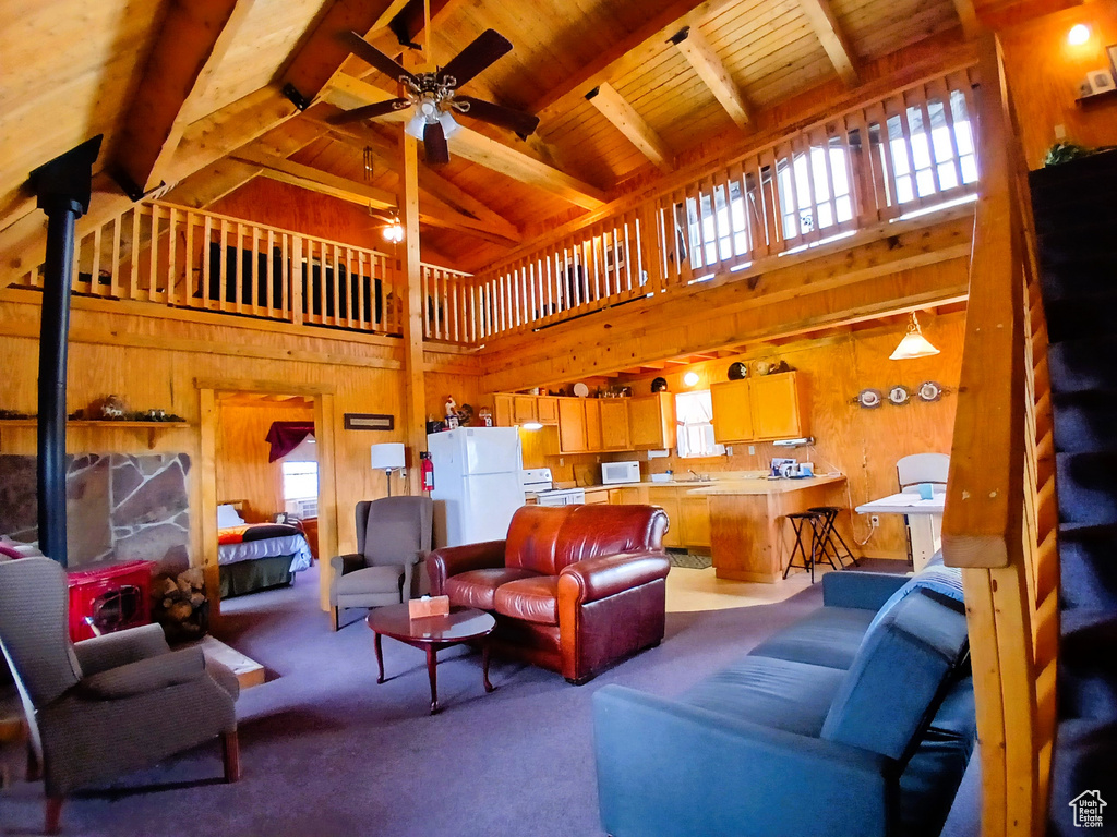 Living room with plenty of natural light, wood walls, high vaulted ceiling, ceiling fan, and a wood stove