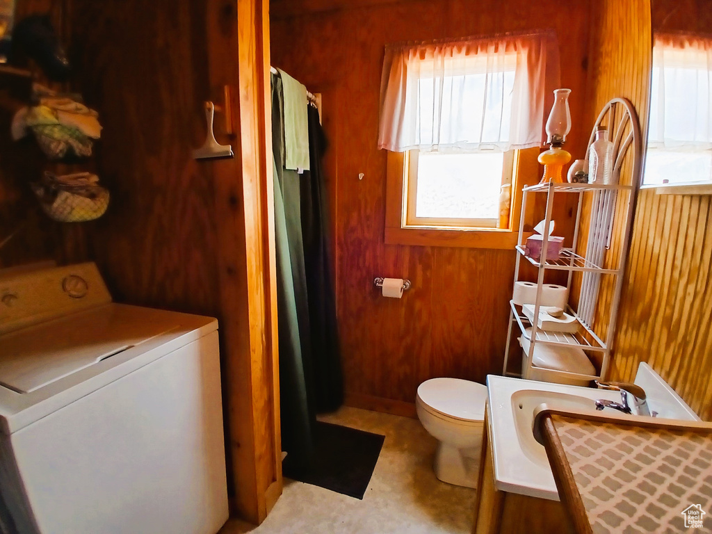 Bathroom featuring washer / dryer, healthy amount of natural light, toilet, wood walls, and curtained shower