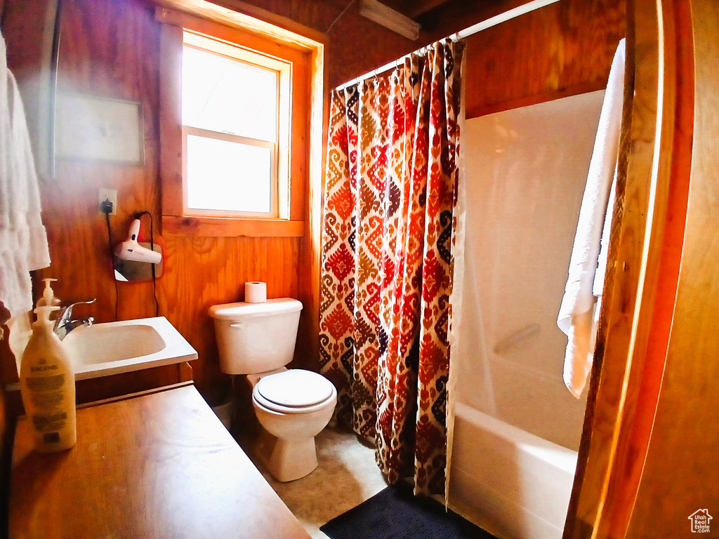 Bathroom featuring toilet, vanity, shower / bath combination with curtain, and wooden walls