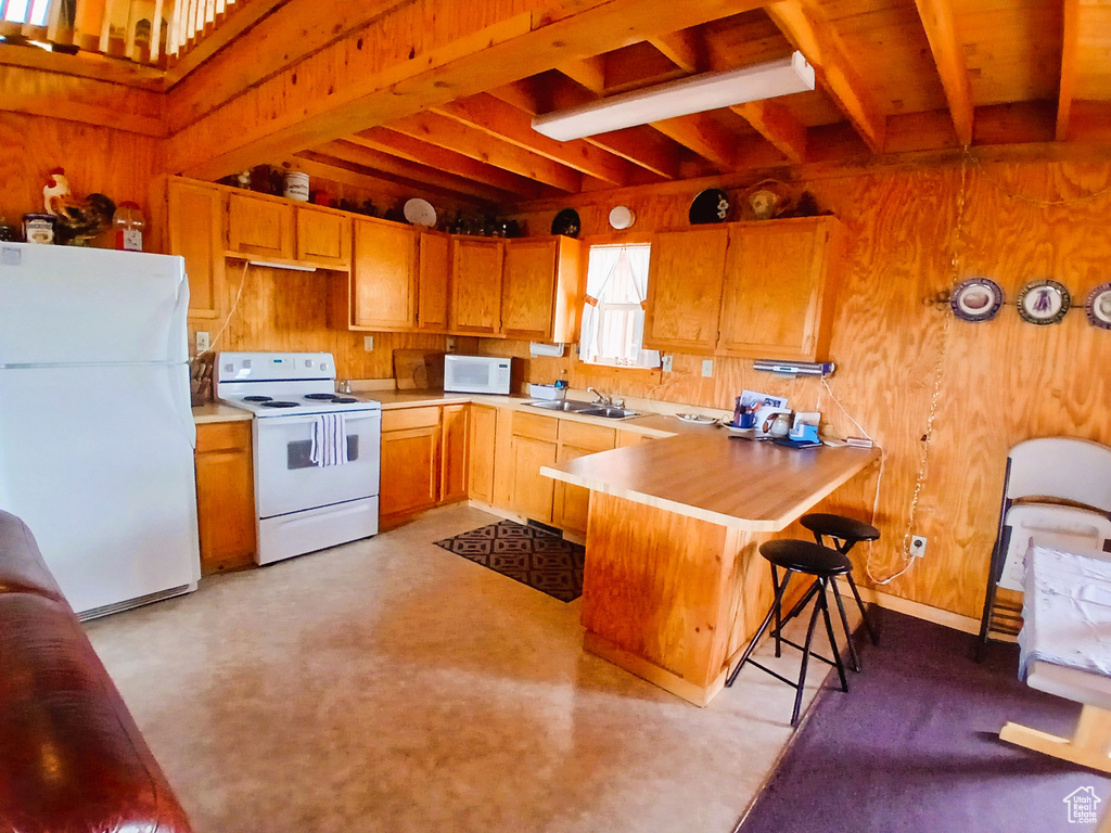 Kitchen with white appliances, beam ceiling, a peninsula, wooden walls, and light countertops