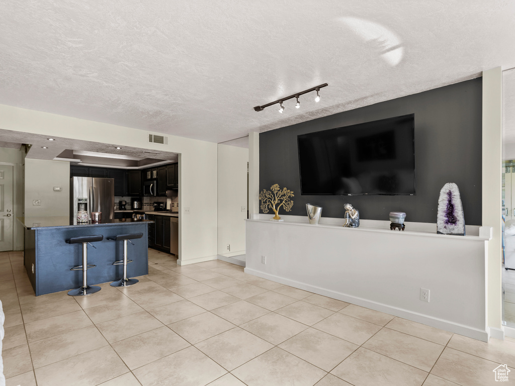 Kitchen featuring stainless steel fridge, open floor plan, light tile patterned flooring, a textured ceiling, and a kitchen bar