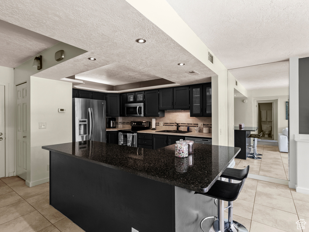 Kitchen with appliances with stainless steel finishes, dark cabinets, a textured ceiling, a sink, and light tile patterned floors