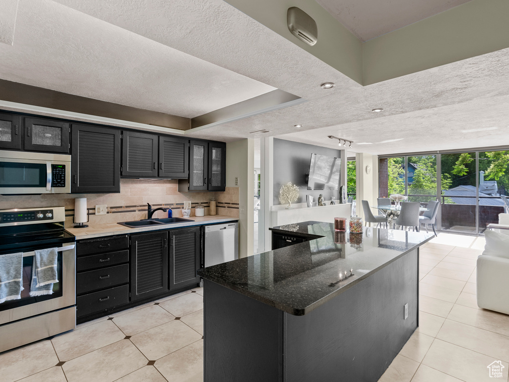 Kitchen with stainless steel appliances, a sink, dark cabinets, light tile patterned floors, and a textured ceiling