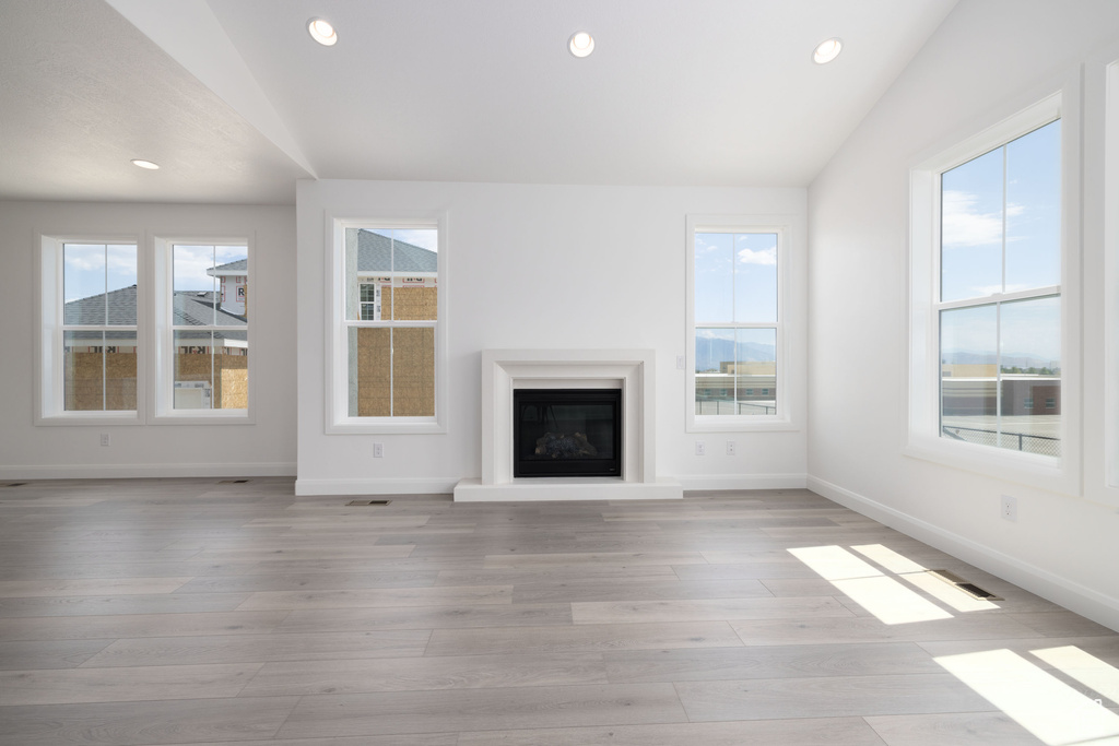 Unfurnished living room featuring baseboards, light wood finished floors, recessed lighting, a glass covered fireplace, and lofted ceiling