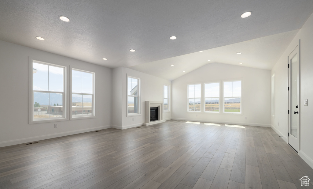 Unfurnished living room with a glass covered fireplace, lofted ceiling, recessed lighting, baseboards, and wood finished floors
