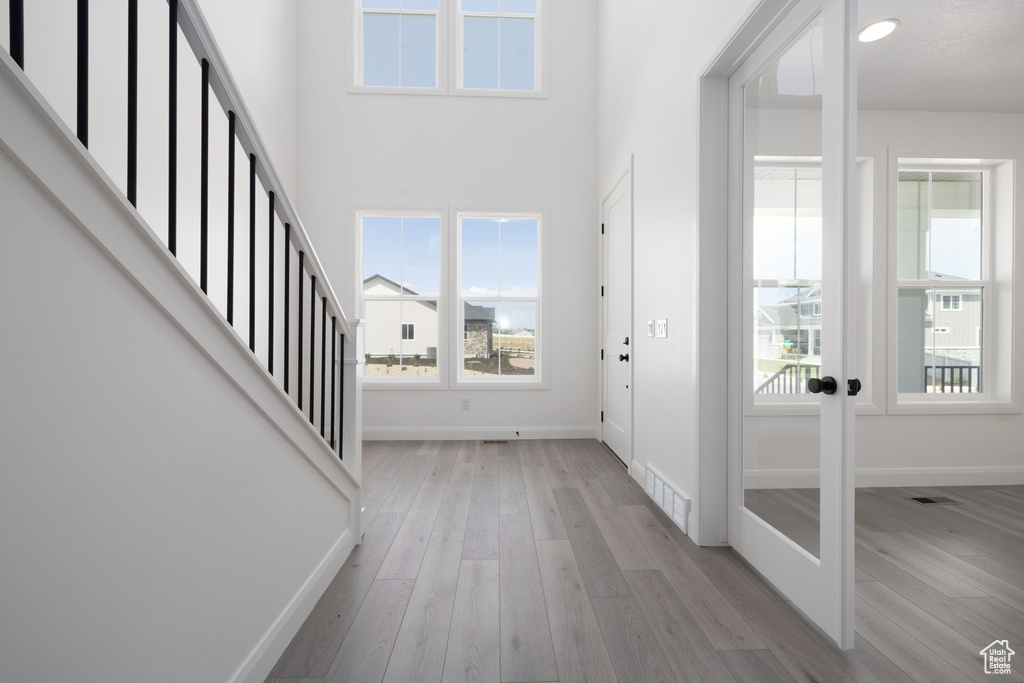 Entryway featuring light wood-style flooring, baseboards, french doors, stairway, and a high ceiling