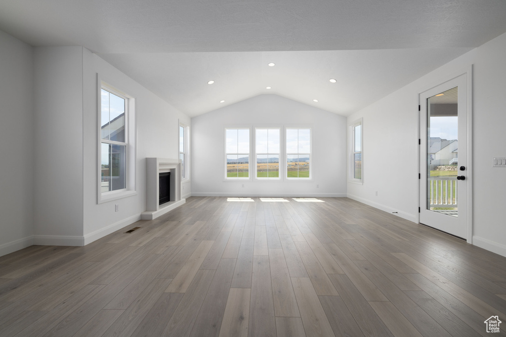 Unfurnished living room with lofted ceiling, a fireplace with raised hearth, wood finished floors, baseboards, and recessed lighting