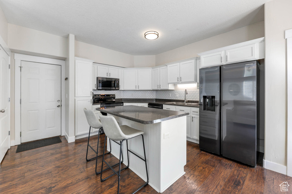 Kitchen featuring appliances with stainless steel finishes, a sink, dark countertops, a breakfast bar area, and white cabinets