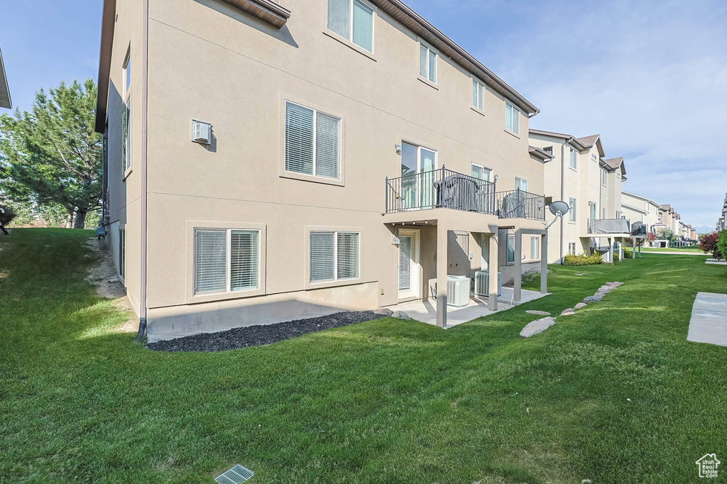 Back of house featuring a lawn, a patio, stucco siding, central AC, and a balcony