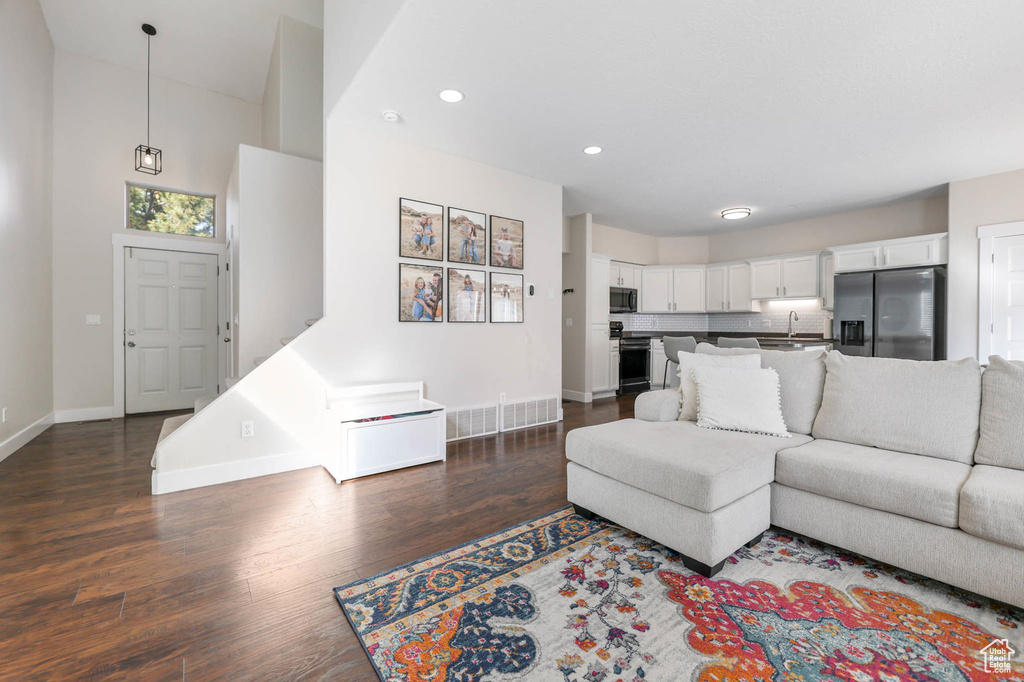 Living area with baseboards, dark wood-type flooring, recessed lighting, and a high ceiling