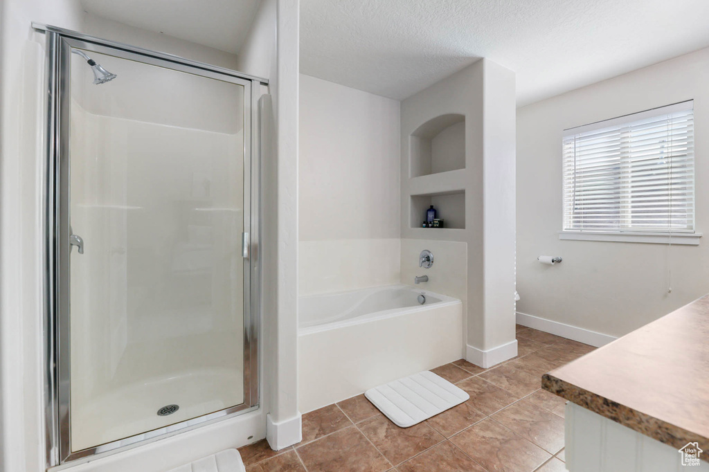 Bathroom featuring a shower stall, a garden tub, vanity, tile patterned flooring, and baseboards