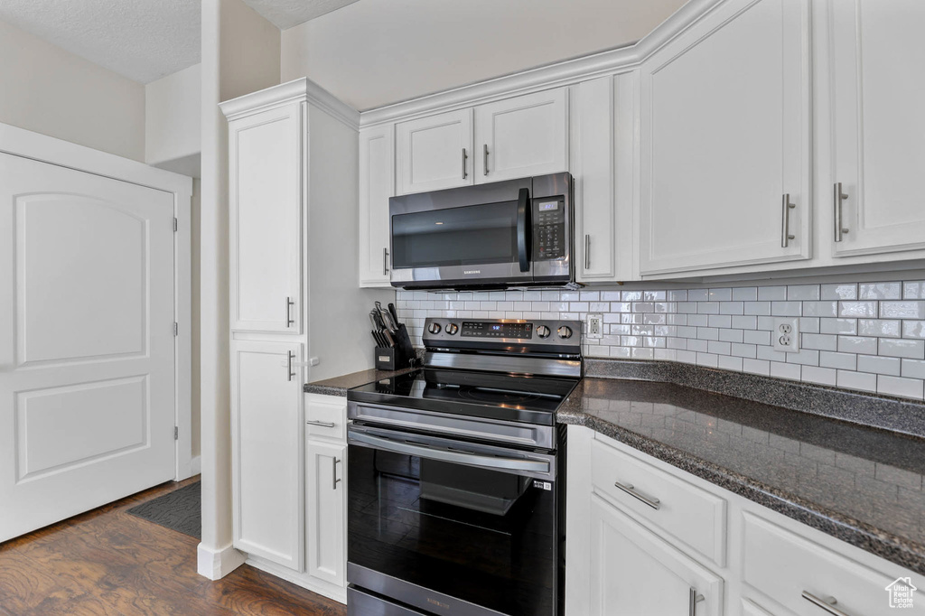 Kitchen featuring stainless steel electric stove, backsplash, dark wood-style flooring, and white cabinetry
