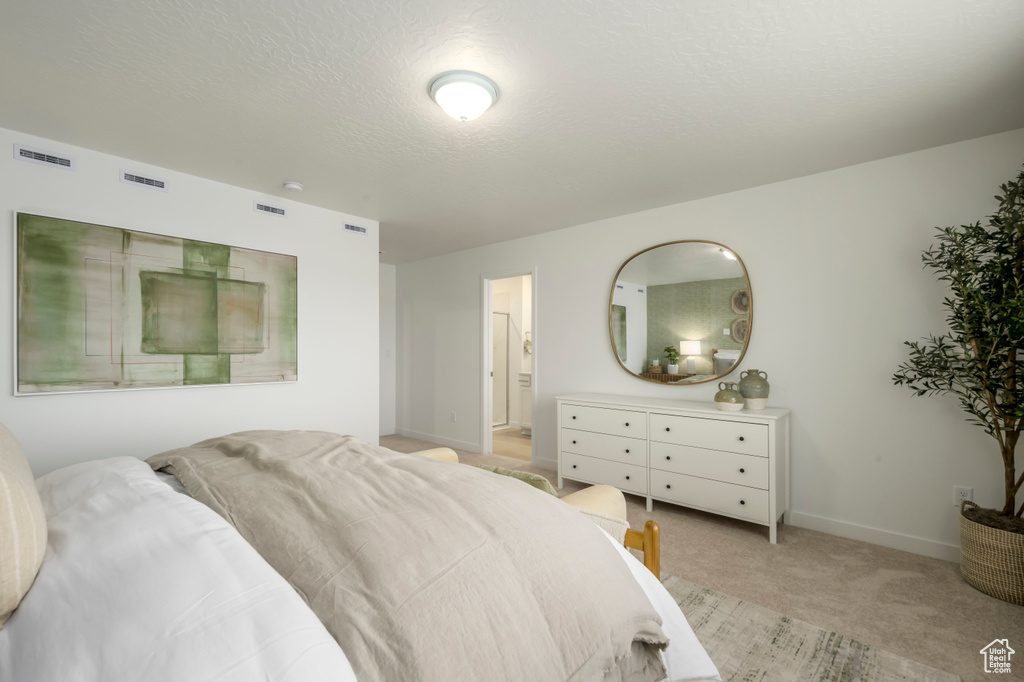 Bedroom with light colored carpet, baseboards, ensuite bathroom, and a textured ceiling