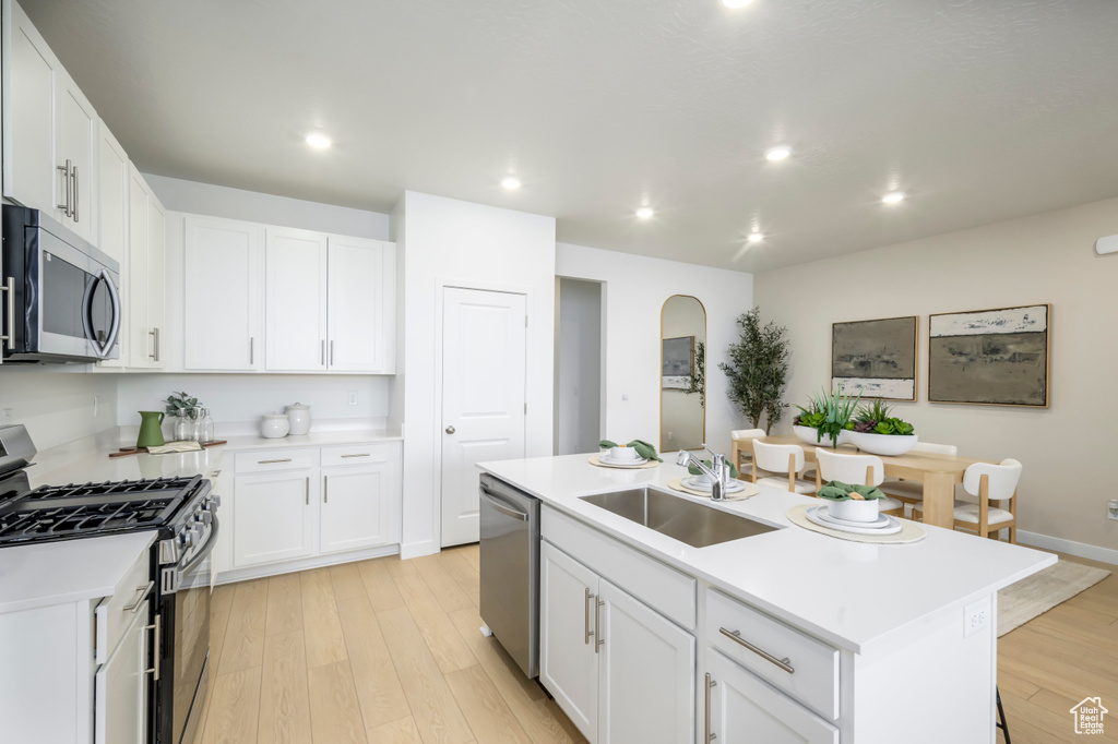 Kitchen with stainless steel appliances, a sink, light wood-style floors, a center island with sink, and white cabinets