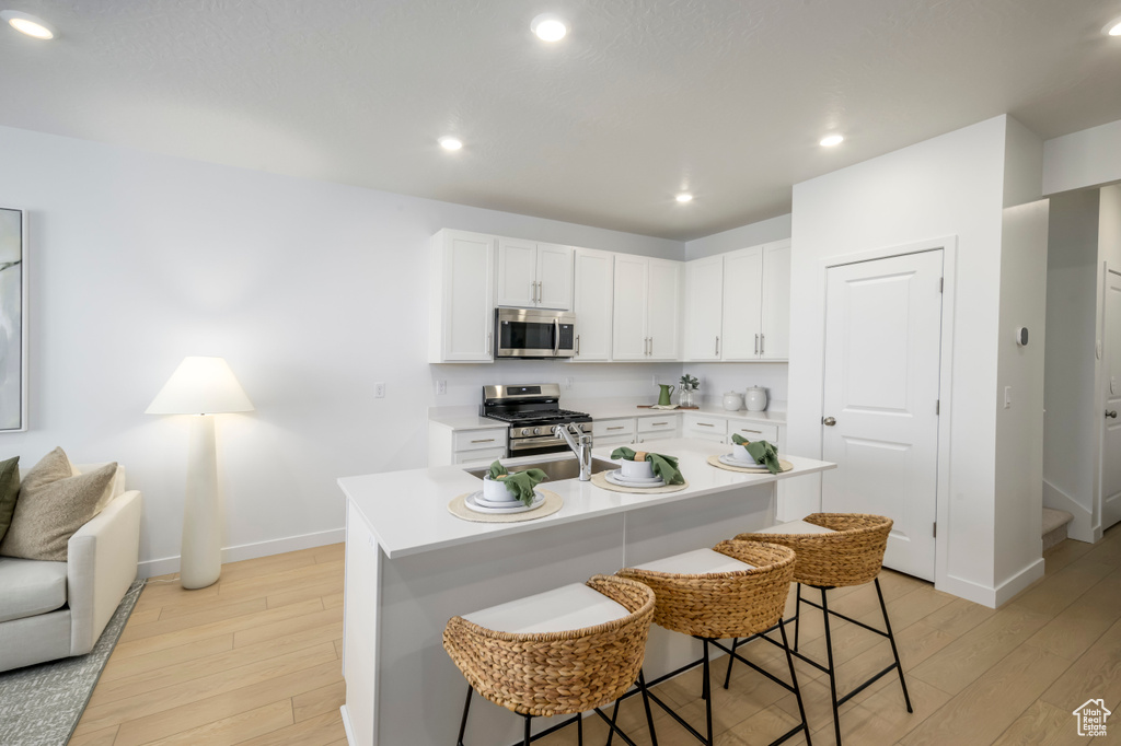 Kitchen with appliances with stainless steel finishes, a kitchen bar, light wood-style floors, baseboards, and light countertops