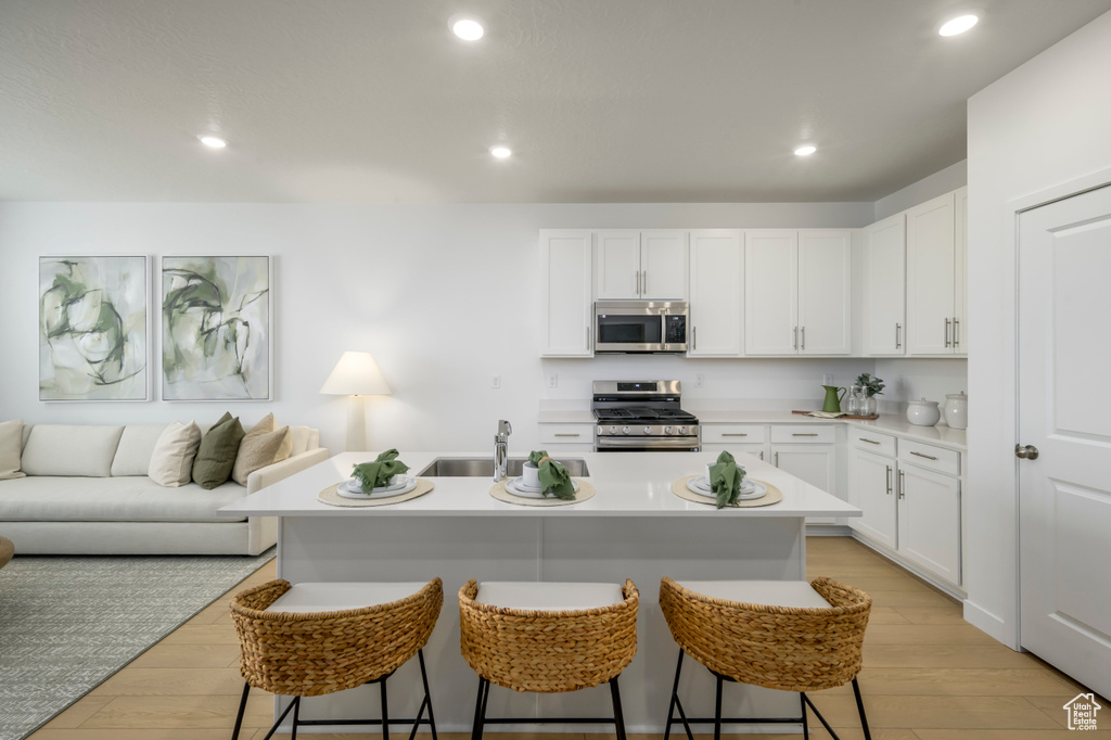 Kitchen with appliances with stainless steel finishes, a sink, a kitchen breakfast bar, open floor plan, and light wood-style flooring