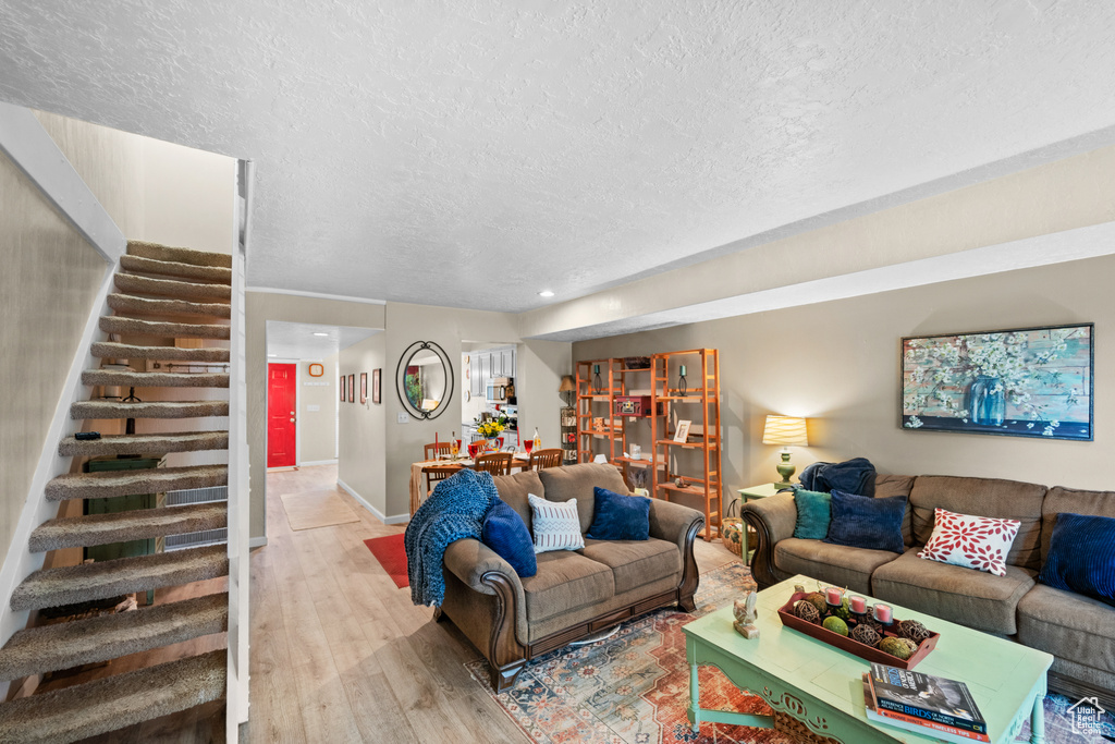 Living room featuring a textured ceiling, stairway, light wood-style floors, baseboards, and recessed lighting