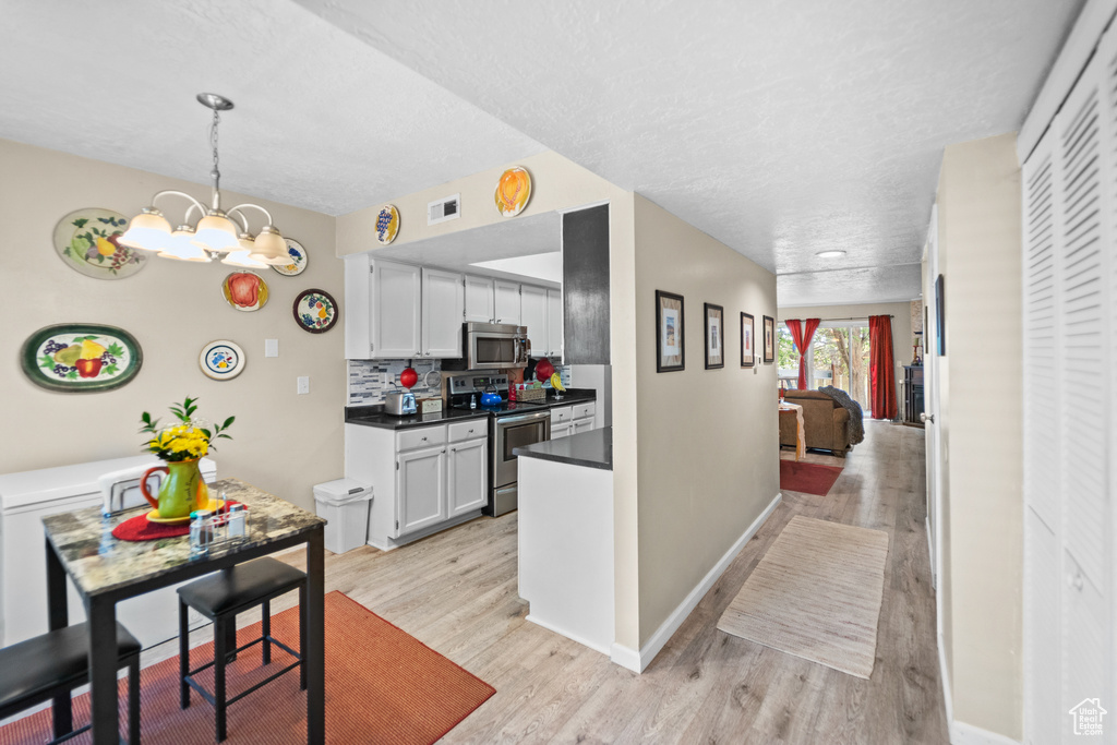 Kitchen featuring stainless steel appliances, light wood finished floors, dark countertops, a textured ceiling, and a chandelier