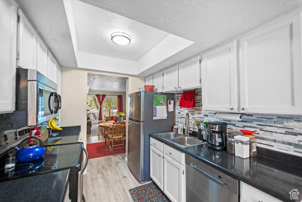 Kitchen featuring stainless steel appliances, a sink, a tray ceiling, white cabinetry, and a textured ceiling