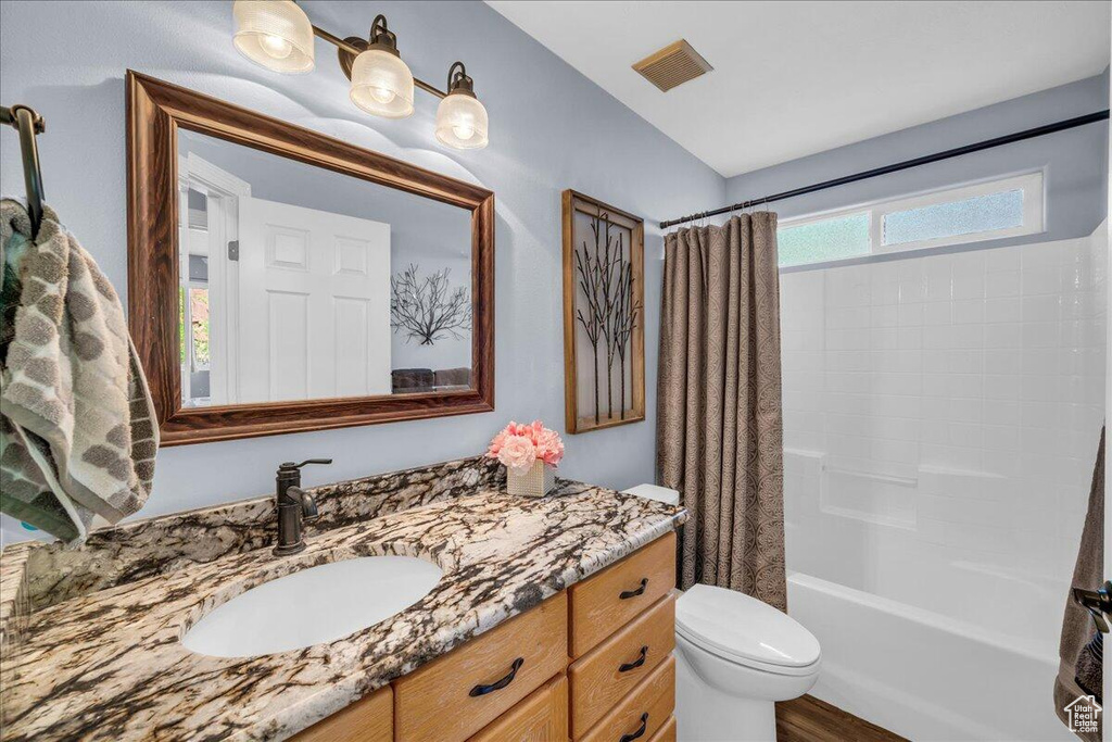 Bathroom featuring vanity, toilet, shower / bath combo, and wood finished floors