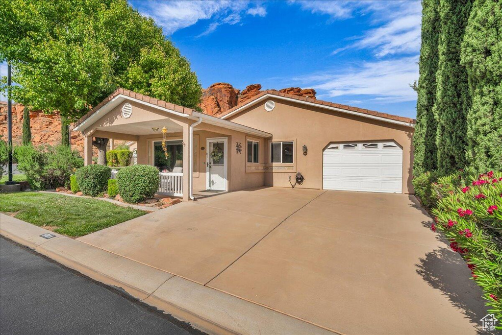 View of front of property featuring covered porch, a garage, stucco siding, a tiled roof, and driveway