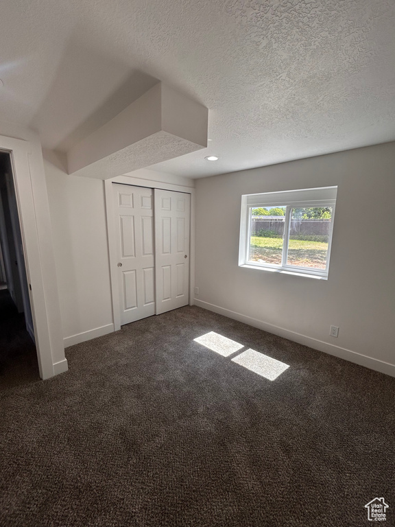 Unfurnished bedroom featuring baseboards, dark carpet, a textured ceiling, a closet, and recessed lighting