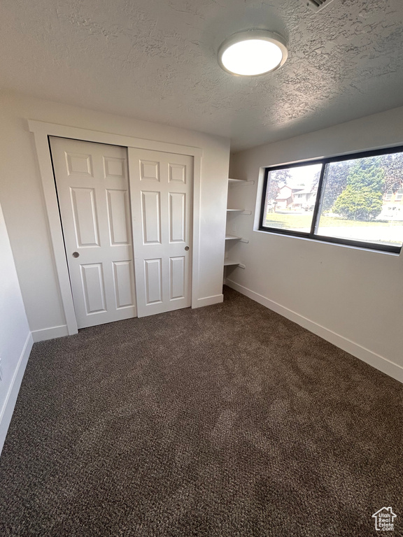 Unfurnished bedroom with a textured ceiling, baseboards, a closet, and dark carpet