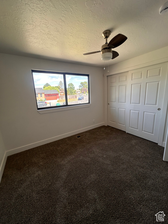 Unfurnished bedroom featuring dark colored carpet, a textured ceiling, baseboards, a closet, and ceiling fan