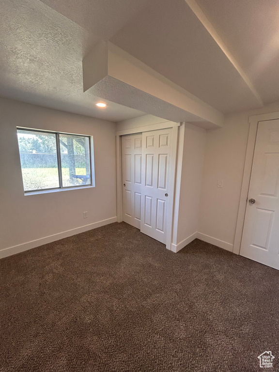 Unfurnished bedroom with dark colored carpet, baseboards, a closet, and a textured ceiling