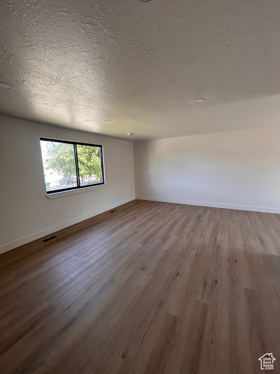 Unfurnished room featuring a textured ceiling, wood finished floors, and baseboards