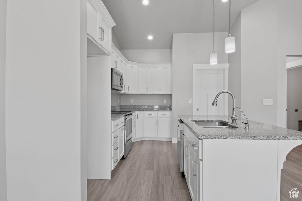 Kitchen with stainless steel appliances, a sink, light wood-type flooring, a kitchen island with sink, and light stone counters
