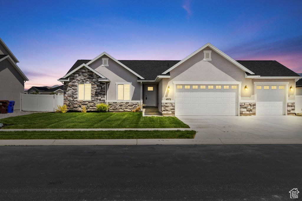View of front of house featuring an attached garage, stone siding, driveway, stucco siding, and roof with shingles