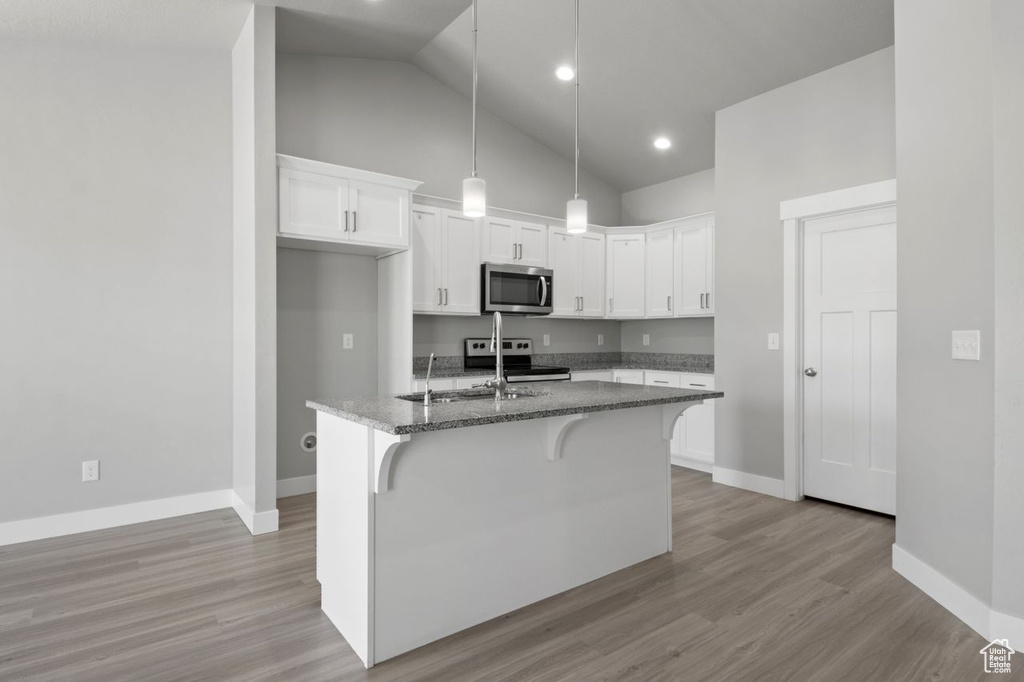 Kitchen featuring stainless steel appliances, a sink, dark stone counters, white cabinets, and a kitchen breakfast bar