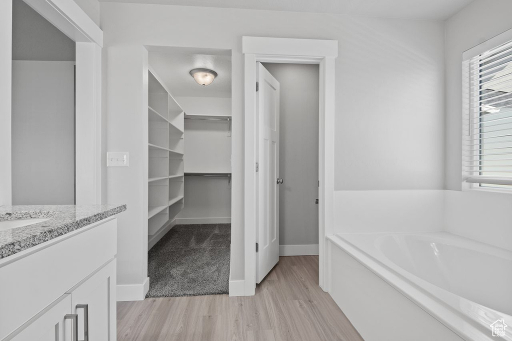Full bathroom with wood finished floors, a bath, vanity, a walk in closet, and baseboards