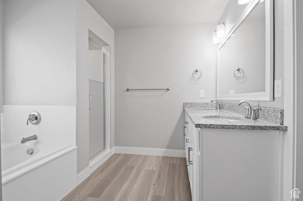 Full bathroom with wood finished floors, double vanity, a bath, baseboards, and a shower with shower door